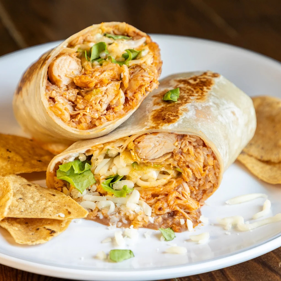 Two halves of a Crazy King Burrito, filled with chicken, rice, cheese, and lettuce, served with tortilla chips.