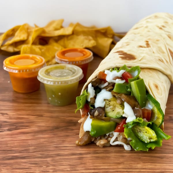 A Crazy King Burrito, filled with vegetables and sour cream, next to tortilla chips and three salsa cups.
