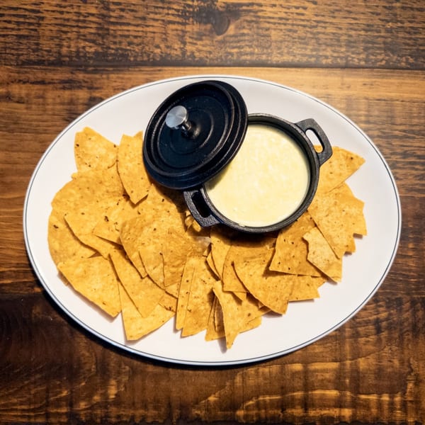 A white plate with a black pot of queso dip and a pile of tortilla chips.