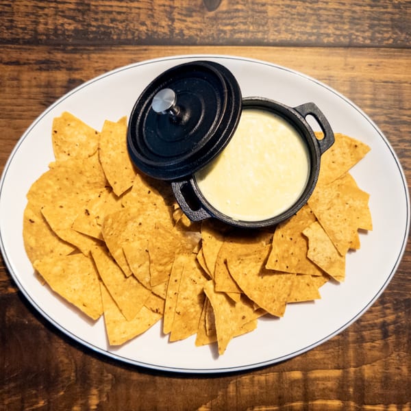 A white plate of tortilla chips with a black cast iron pot of queso dip.